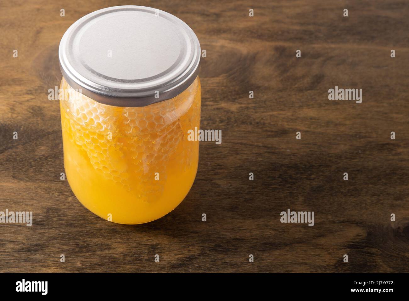 Vaso di miele con nido d'ape. Prodotto di ape trasparente giallo. Confezione da mezzo litro con spazio per un'etichetta. Sfondo in legno. Miele di ape in un vaso di vetro. Cibo sano naturale. Spazio di copia. Foto Stock