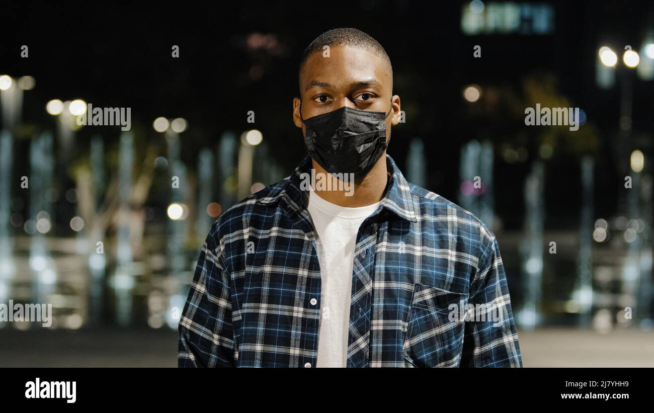 African american uomo fiducioso uomo uomo indossa maschera medica in piedi nella città di notte guardando la macchina fotografica dimostra di mostrare il testo di cartone nessuna vaccinazione Foto Stock