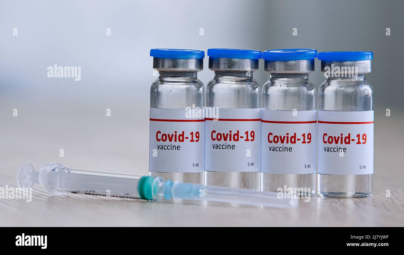 Primo piano di quattro bottiglie di vetro con farmaco vaccino contro il virus covid-19 rimedio per l'epidemia di immunizzazione del coronavirus stand su tavola di legno in Foto Stock