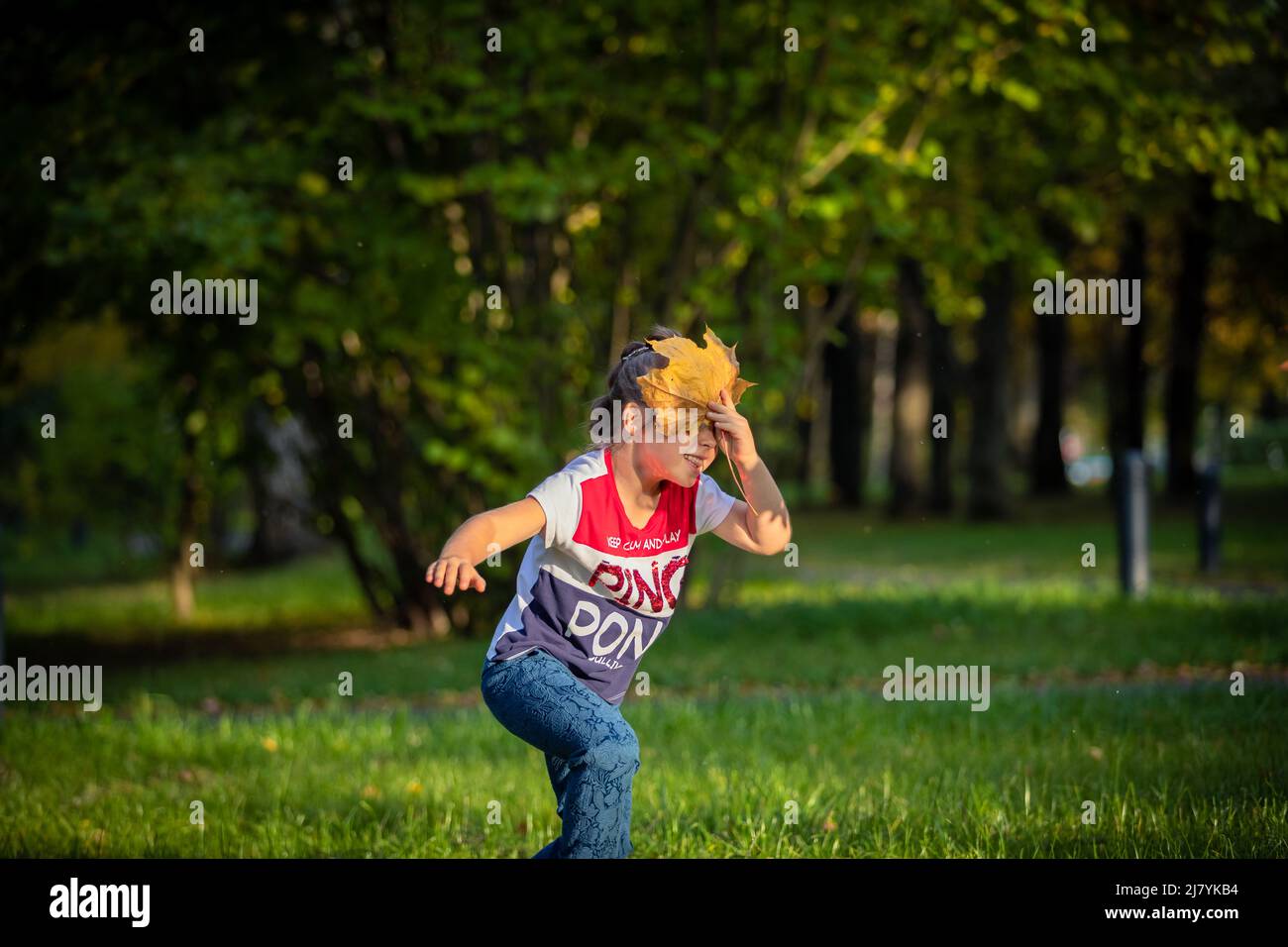 Ragazza ride e gioca con le foglie nel parco in estate. Foto Stock