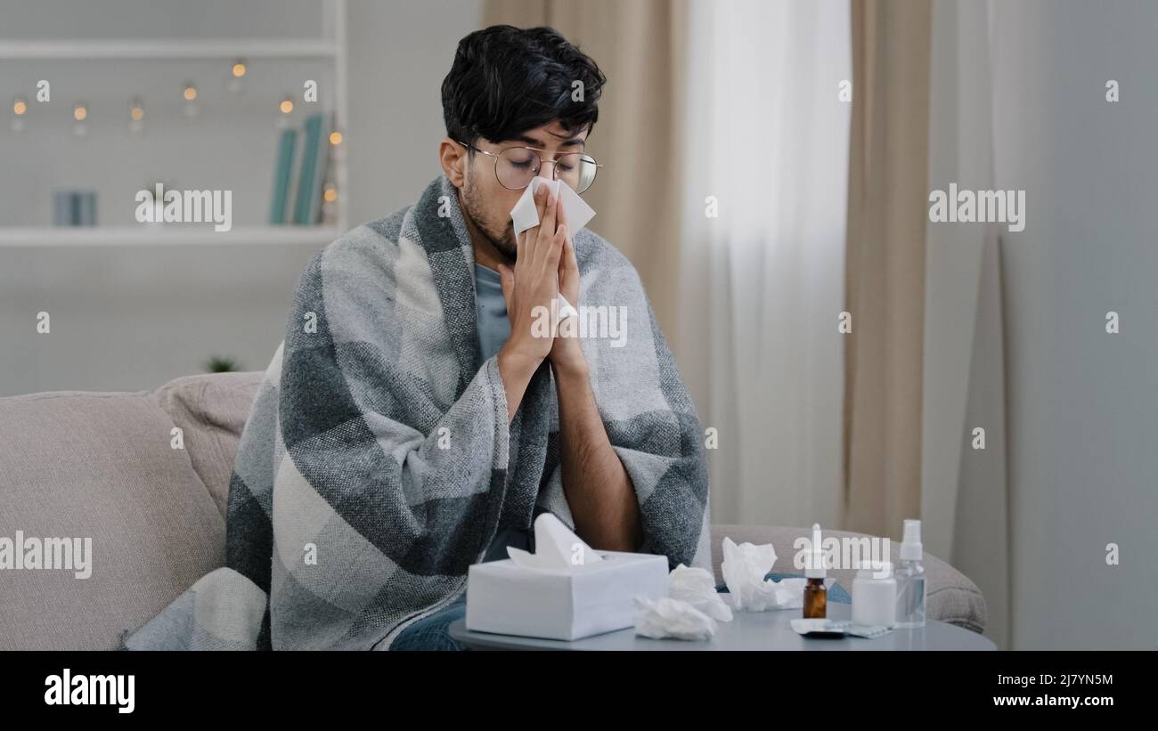 Arabo bearded malato triste uomo con occhiali siede sul divano a casa soffre di naso che cola influenza malattia coronavirus pandemic covid epidemia starnuti. Non bene Foto Stock