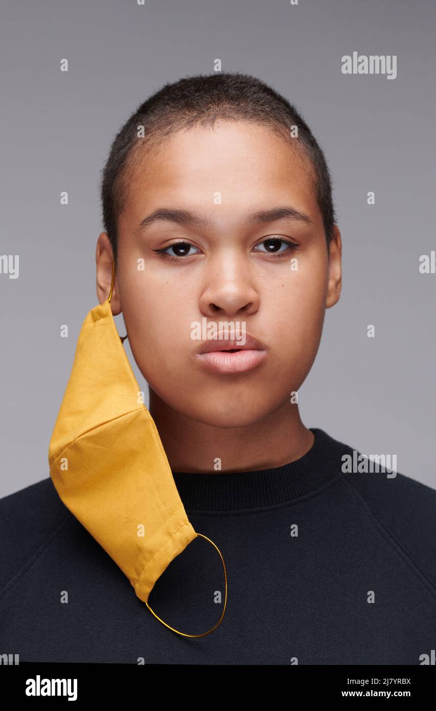 Ritratto della giovane donna afro-americana seria con buzz taglio utilizzando maschera facciale gialla per la protezione, concetto di coronavirus Foto Stock