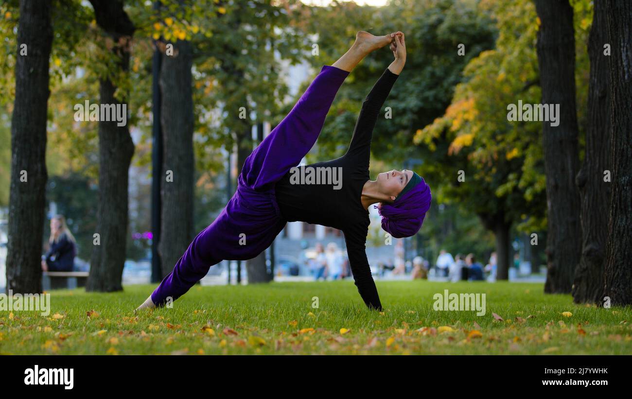 Forte sportiva ragazza islamica in hijab yoga insegnante donna si alza in fianco su erba in parco facendo Ardhachandrasana Vasishthasana posa Foto Stock