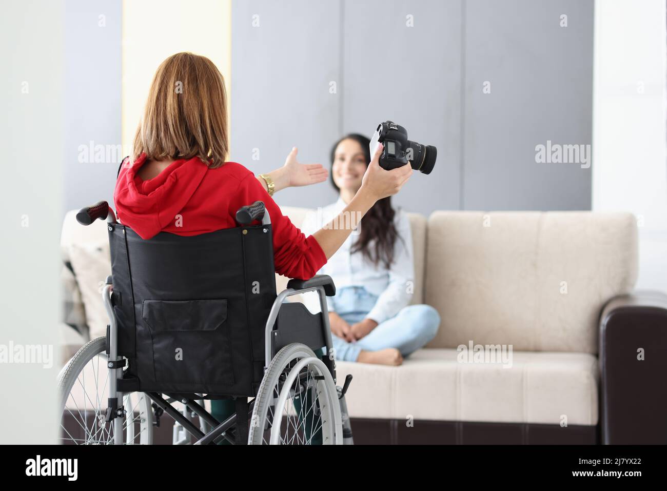 Fotografo professionista in sedia a rotelle dare consigli su posare per modellare sul divano Foto Stock