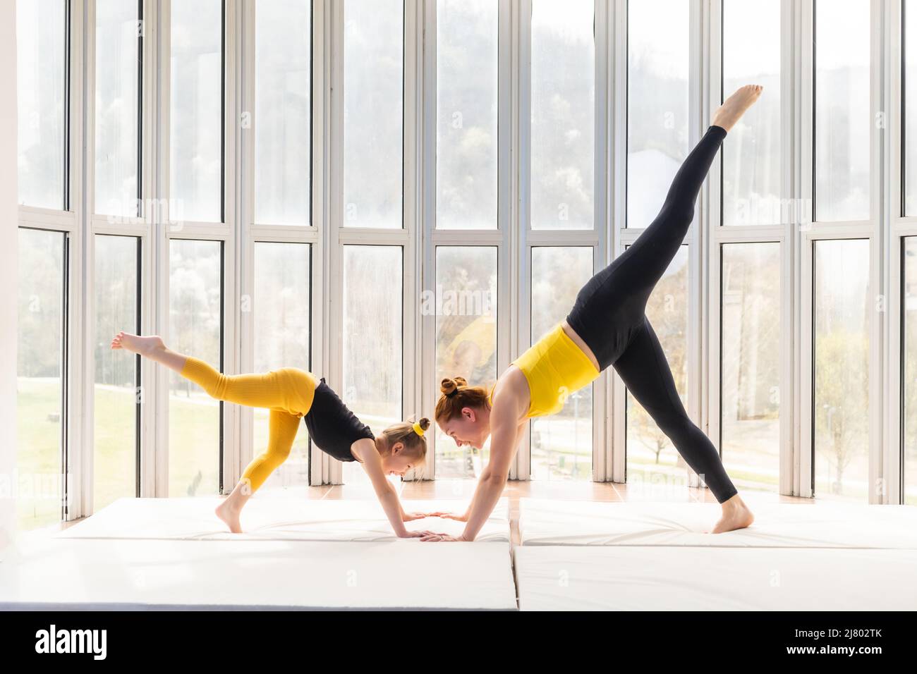 Giovane madre e figlia che praticano lo yoga insieme. Cane rivolto verso il basso a tre zampe Foto Stock