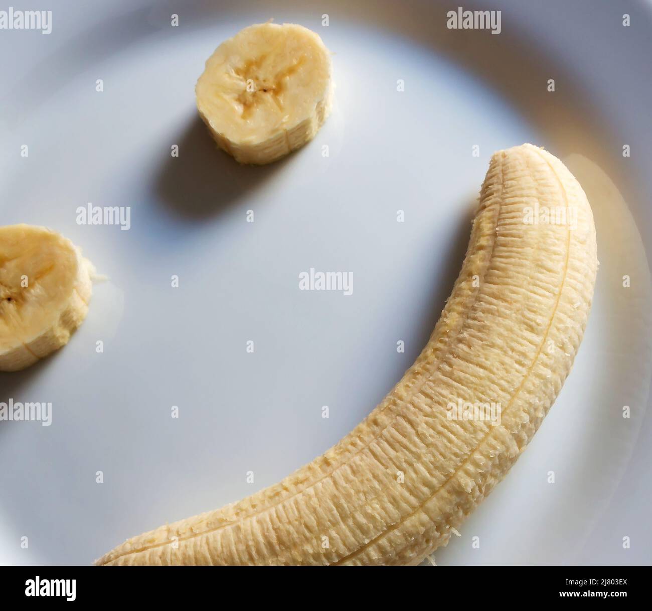 Parte di faccia felice formata da banana grezza su piastra bianca fotografata dall'alto Foto Stock