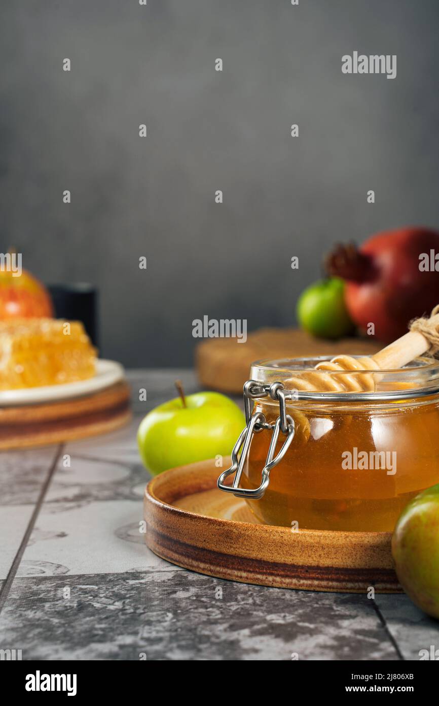 Vaso di vetro con miele fresco, cucchiaio di miele, mela e melograno. Concetto Ebraico Capodanno Happy Holiday Rosh Hashanah. Layout di simboli tradizionali. Foto Stock