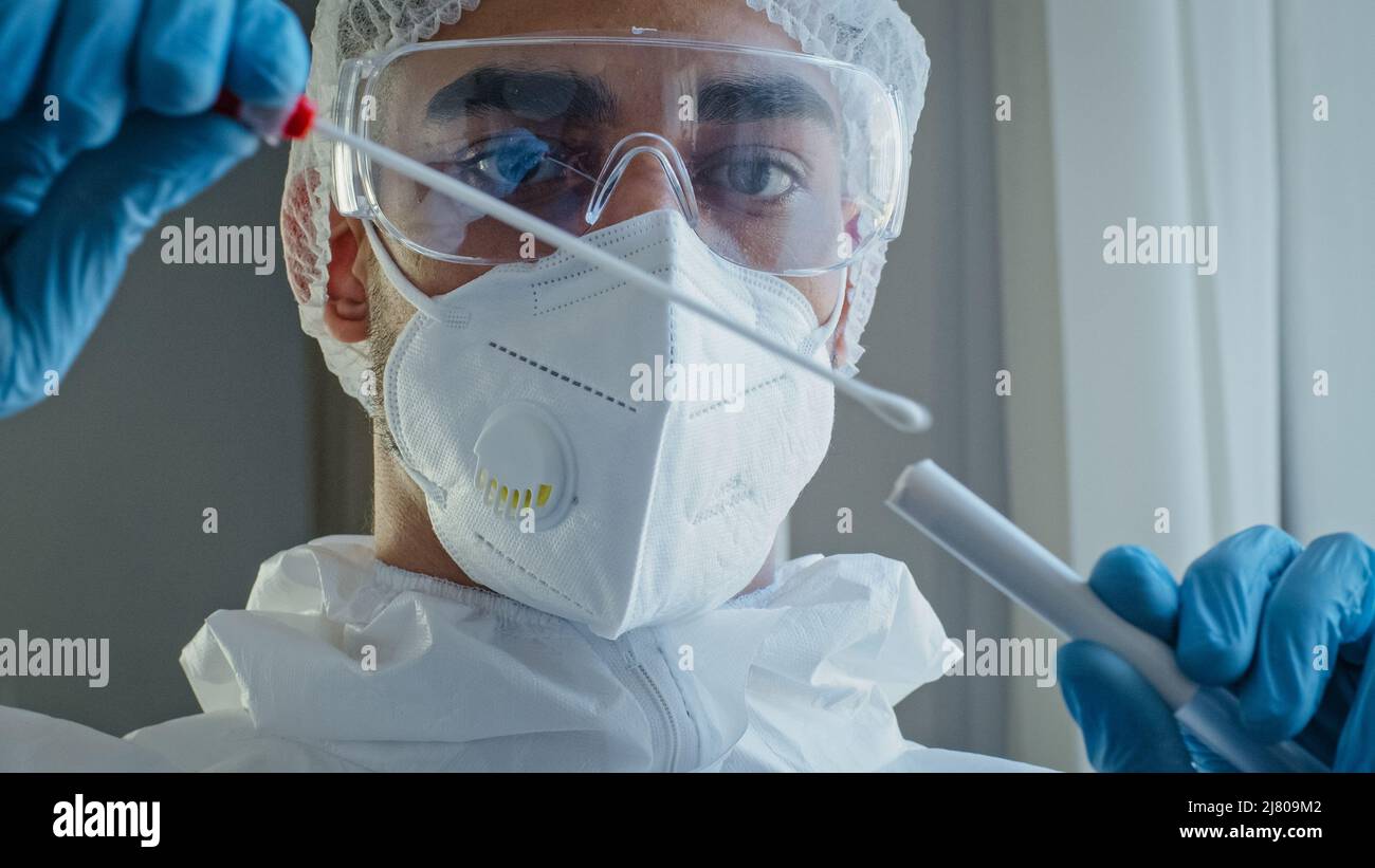 Ritratto arabo ispanico uomo medico medico in tuta protettiva PPE eseguito tampone di congestione da persona irriconoscibile per testare il coronavirus Foto Stock