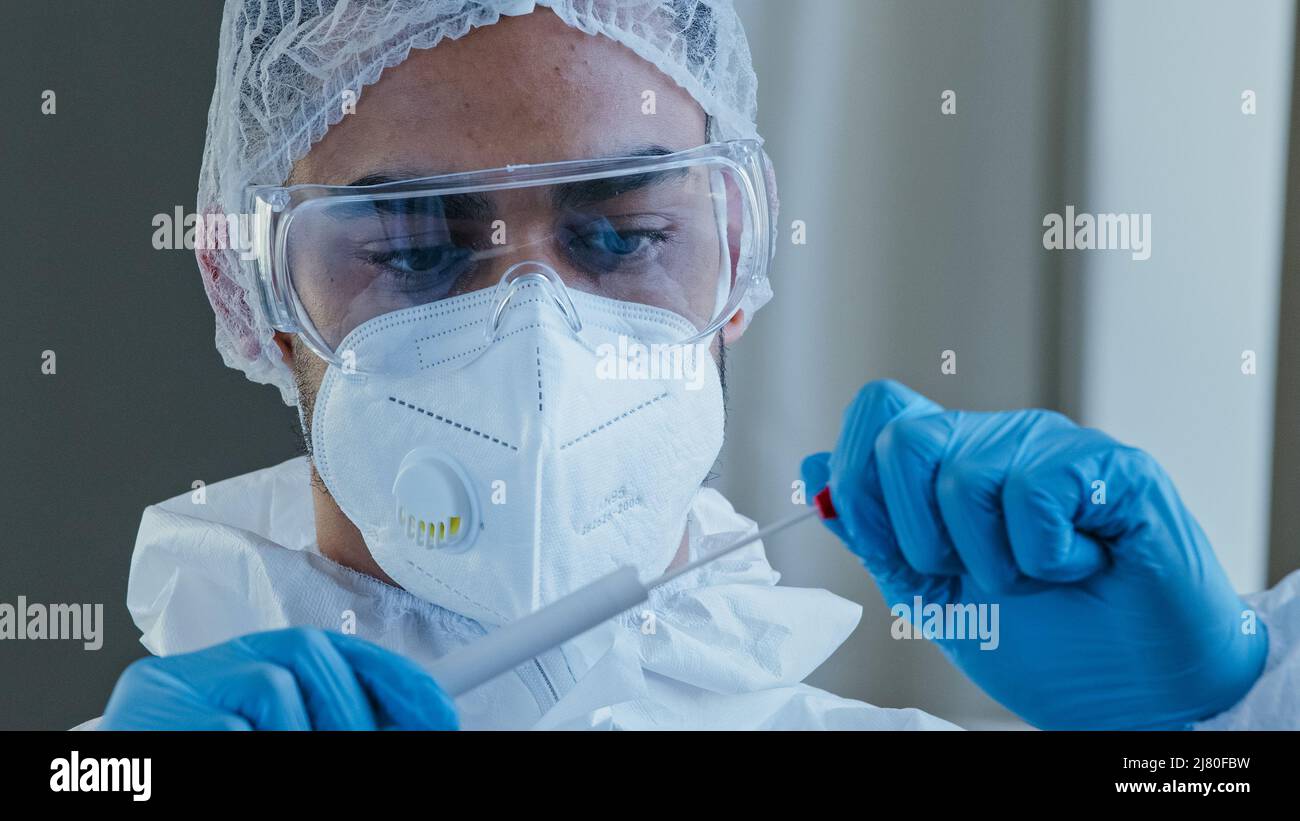 Ritratto arabo ispanico uomo medico medico in tuta protettiva PPE eseguito tampone di congestione da persona irriconoscibile per testare il coronavirus Foto Stock