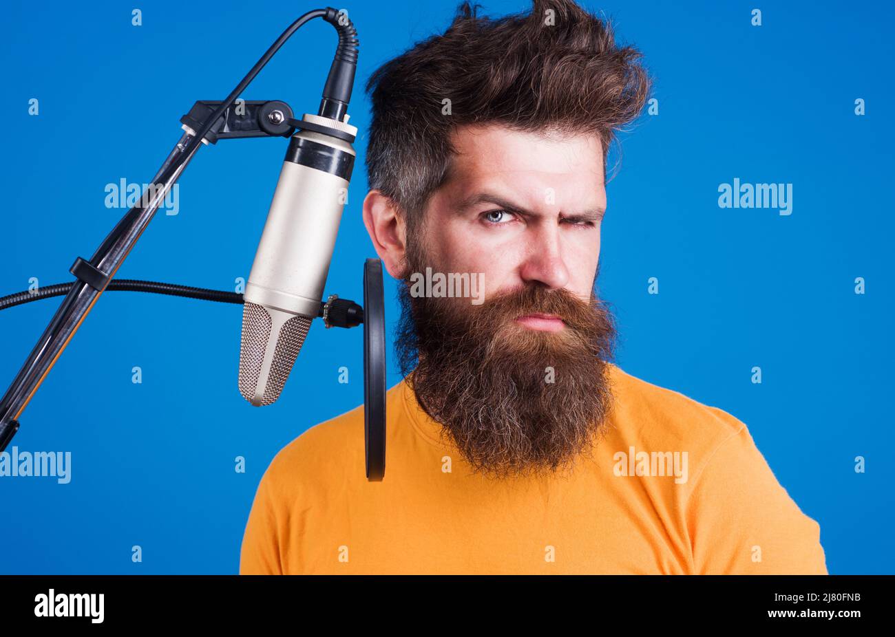 Uomo bearded che cantava nel microfono a condensatore. Cantante professionista maschile. Canto in studio. Karaoke. Foto Stock