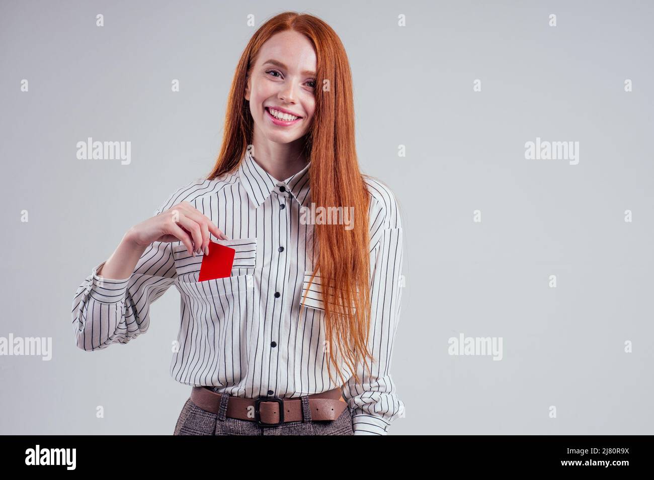 attraente rosso testa caucasica donna d'affari indossando a righe camicia che tiene carta di credito studio bianco sfondo nero venerdì vendita Foto Stock