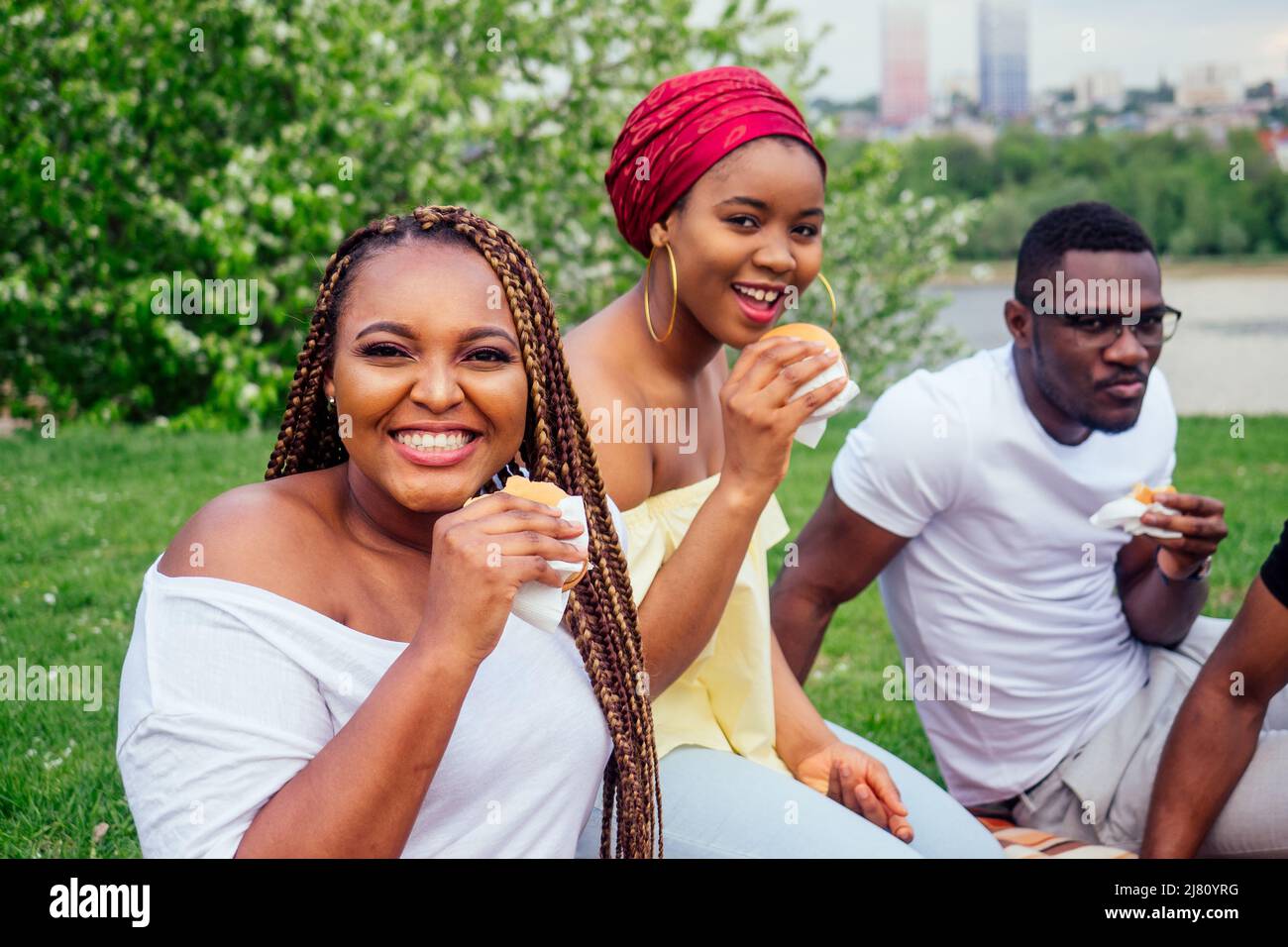 happy casual america africani persone divertirsi e mangiare hamburger all'aperto stile di vita, studenti per una pausa estate sera nuvoloso tempo nel parco Foto Stock