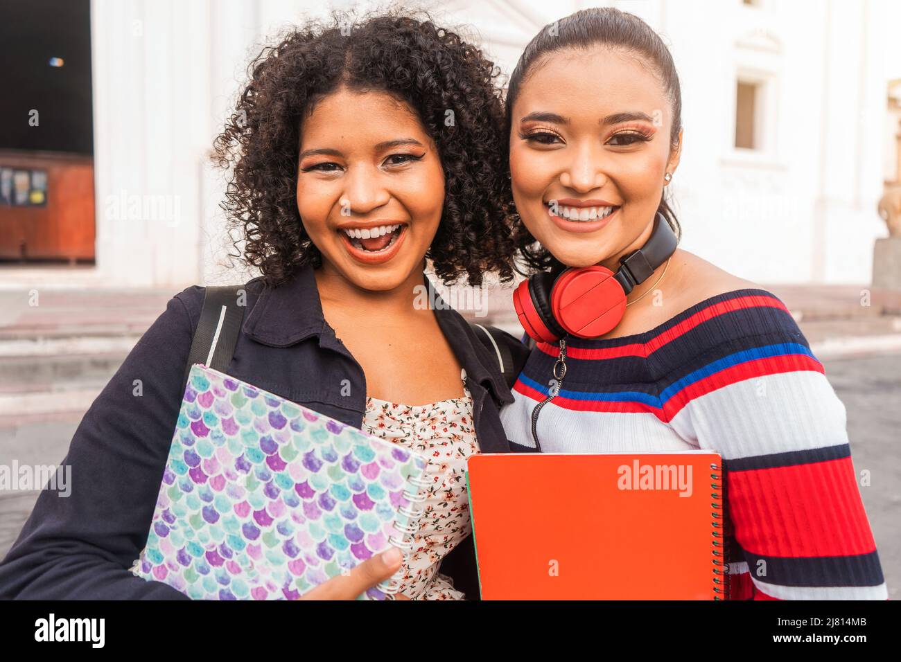 Due studenti latini, un meszo e un ispanico che guardano la macchina fotografica e sorridono tenendo i taccuini nelle mani e uno zaino sulle spalle. Foto Stock