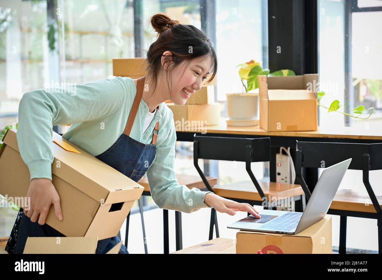 Donna che lavora sodo nel suo negozio, rispondendo alle domande dei clienti sul sito web online e imballando il prodotto di consegna nella scatola. Avvio aziendale co Foto Stock