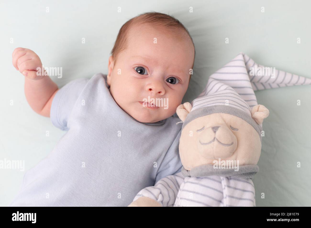 Il bambino è sdraiato in un presepe con un orsacchiotto . Il bambino ha 0-3 mesi. Bambino calmo. Un articolo sui giocattoli per i bambini. Un giocattolo morbido. Spazio copia Foto Stock
