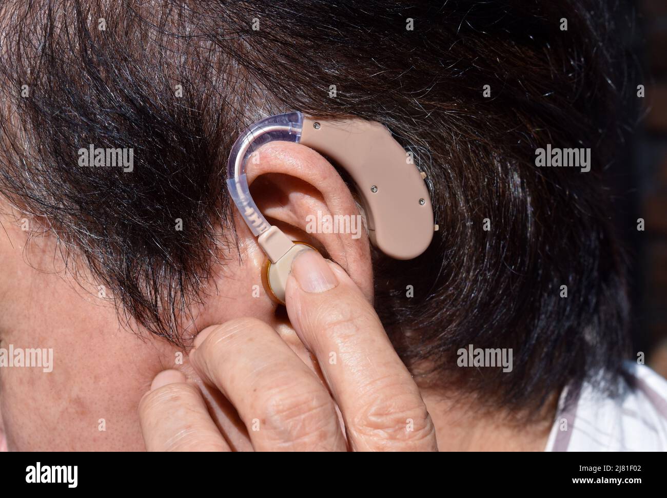 Apparecchio acustico elettronico nell'orecchio del vecchio asiatico con totale sordità. Foto Stock