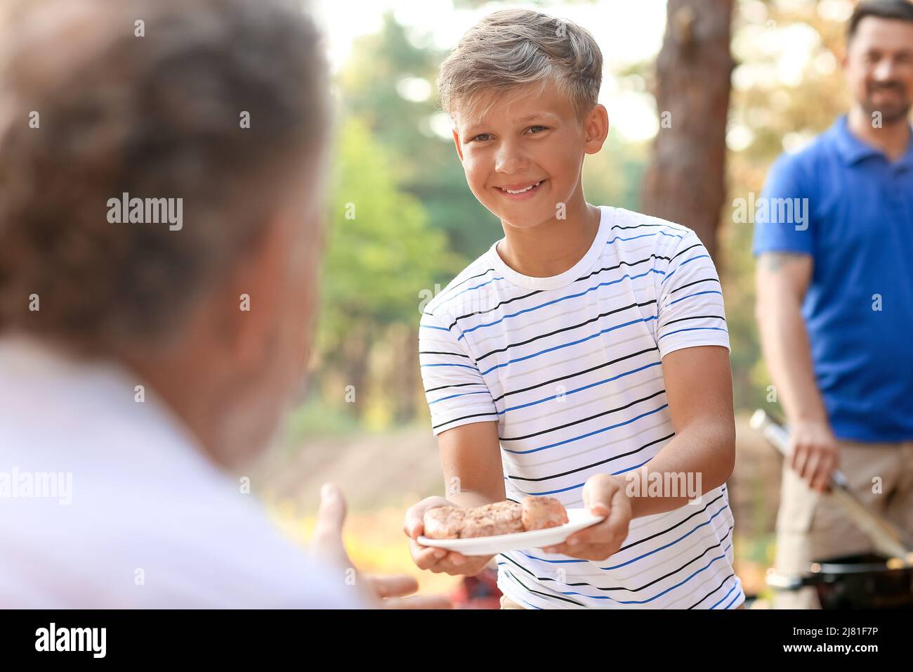 Ragazzino che dà piatto con carne alla griglia al nonno alla festa del barbecue Foto Stock