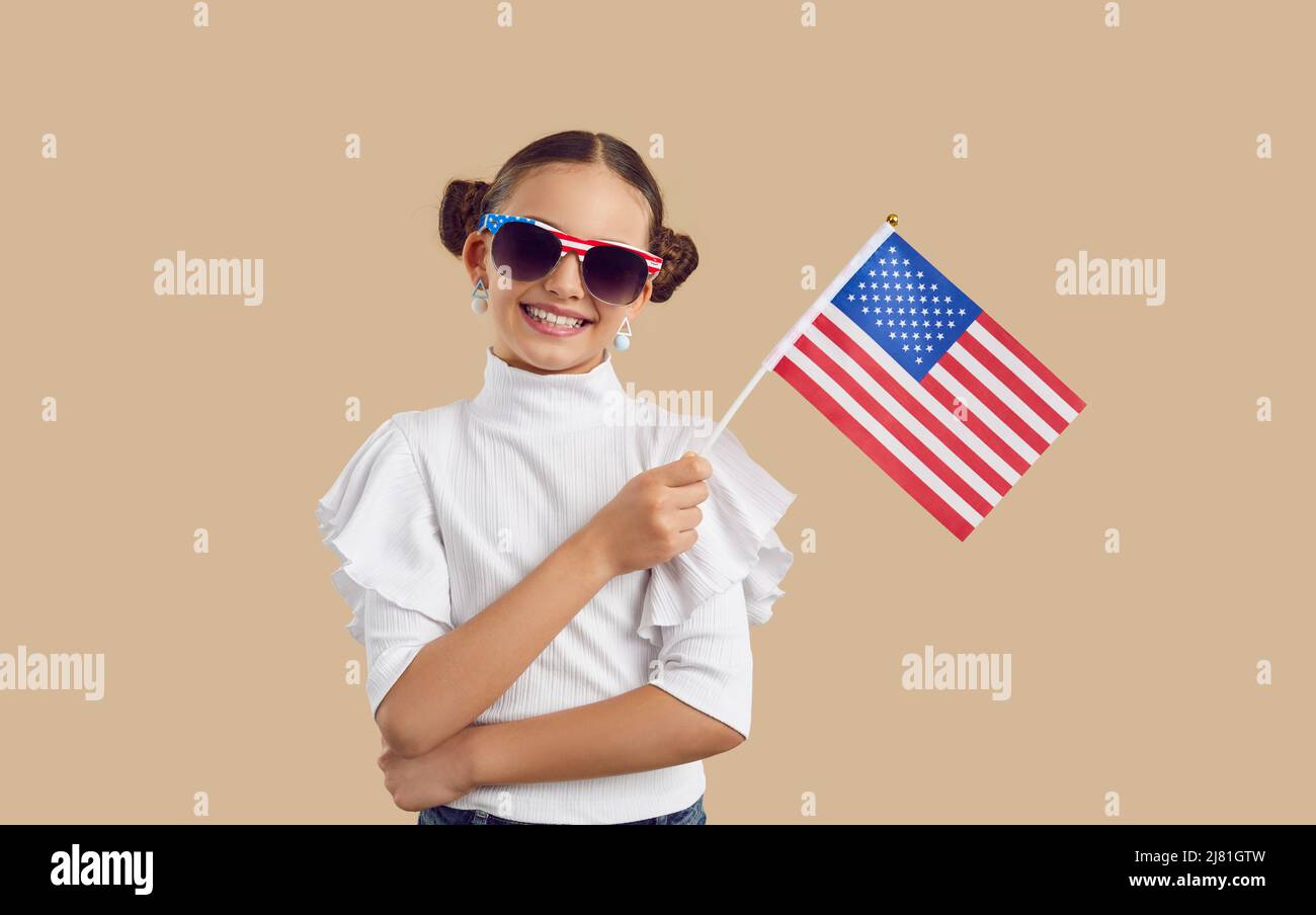 Ritratto di bella ragazza in occhiali da sole in piedi in studio, tenendo bandiera americana e sorridente Foto Stock