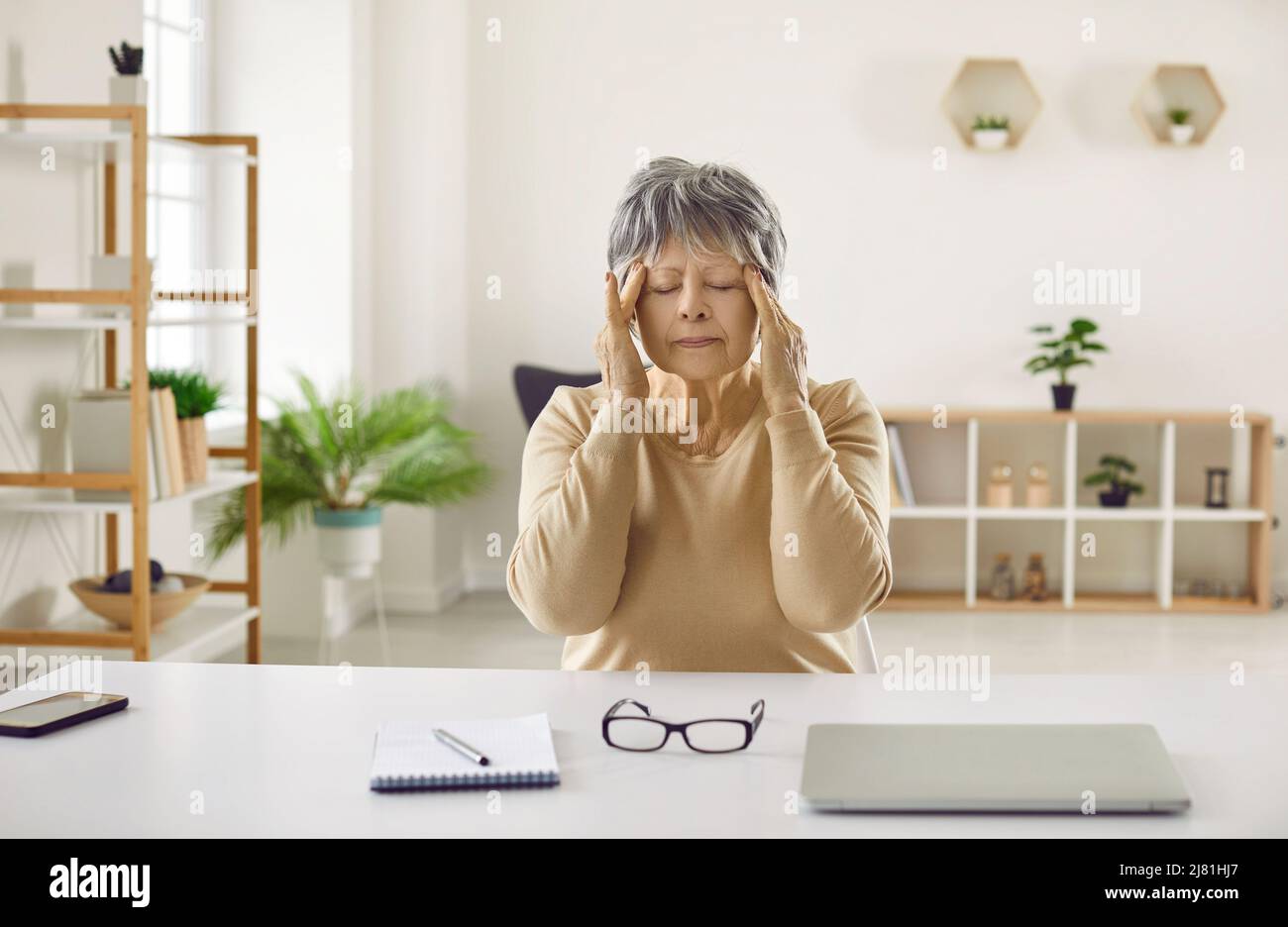 Donna anziana stanca che ha mal di testa dopo aver lavorato sul computer sta facendo il massaggio della testa Foto Stock