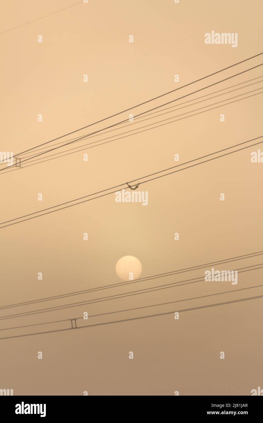 Il sole tramontare è l'equilibrio tra le linee elettriche su un cielo arancione nebbia Foto Stock