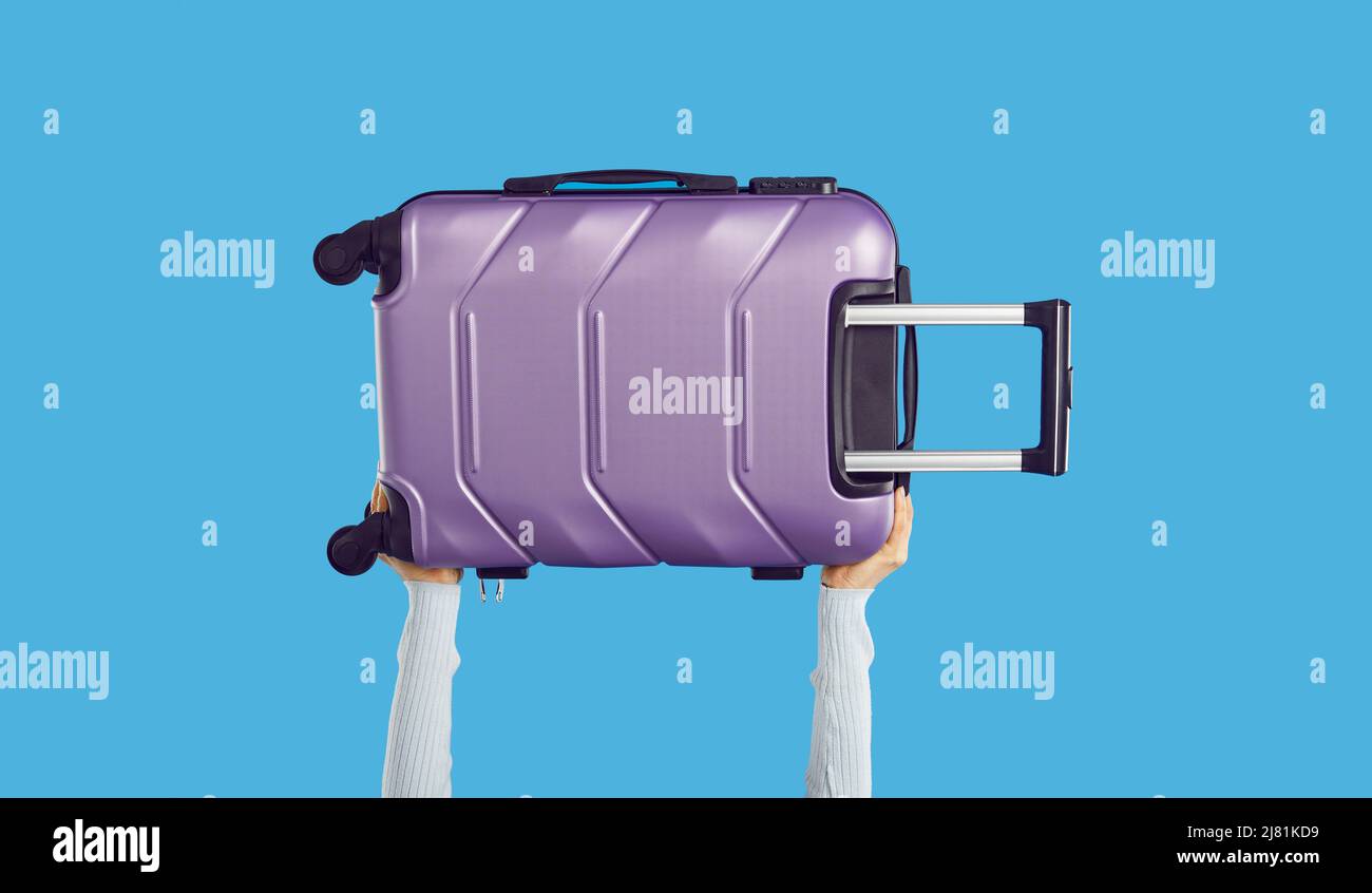 Il viaggiatore tiene una moderna valigia con ruote viola isolata su sfondo di colore blu Foto Stock
