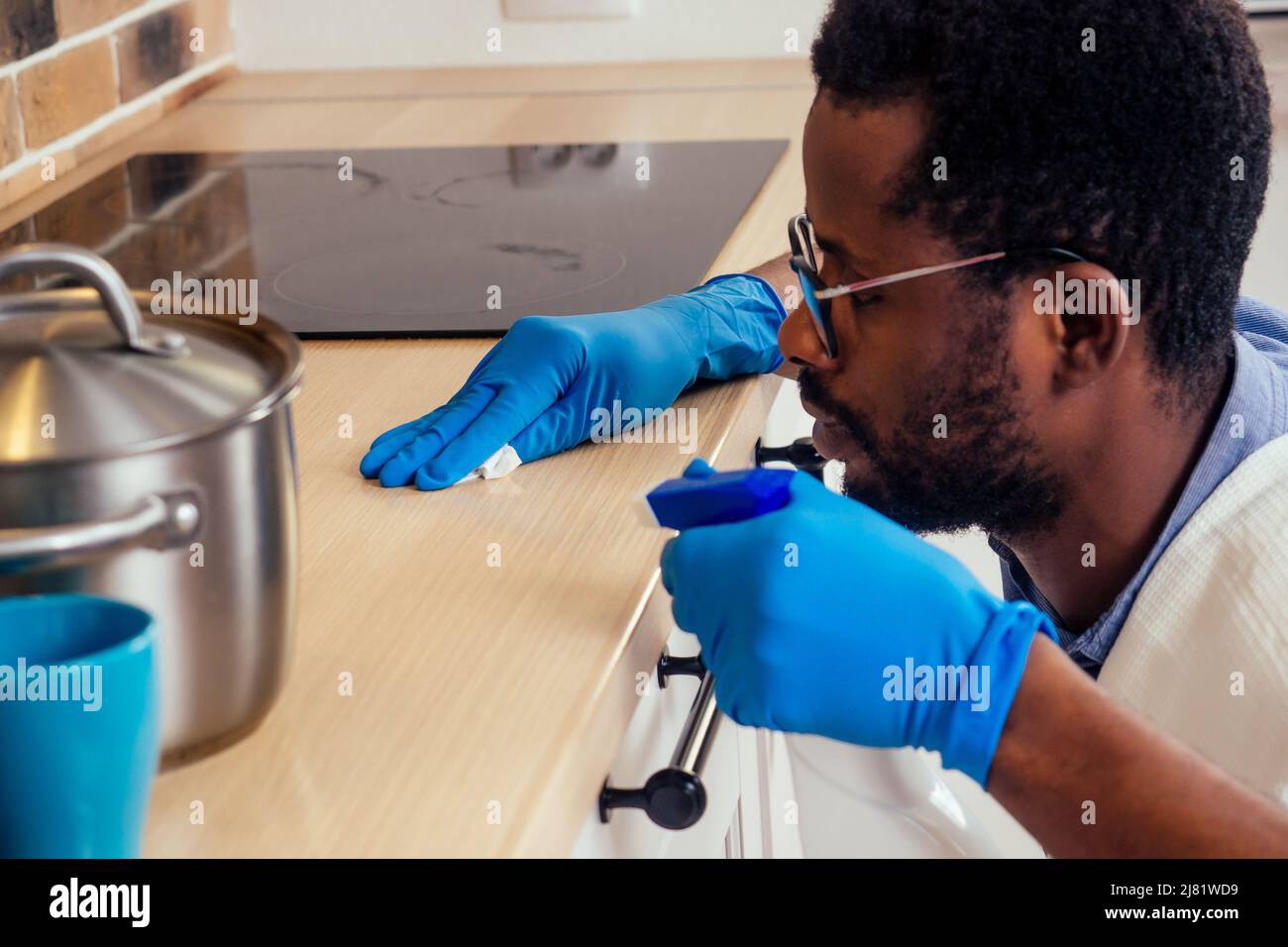 uomo africano pulizia cappa di cottura piano cottura a casa, Brick parete di fondo Foto Stock