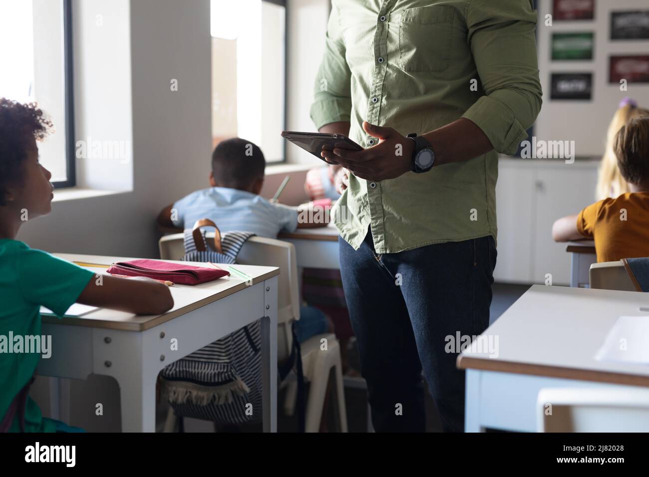 Metà della sezione del giovane insegnante maschile afroamericano con tavoletta digitale che parla con il ragazzo elementare Foto Stock