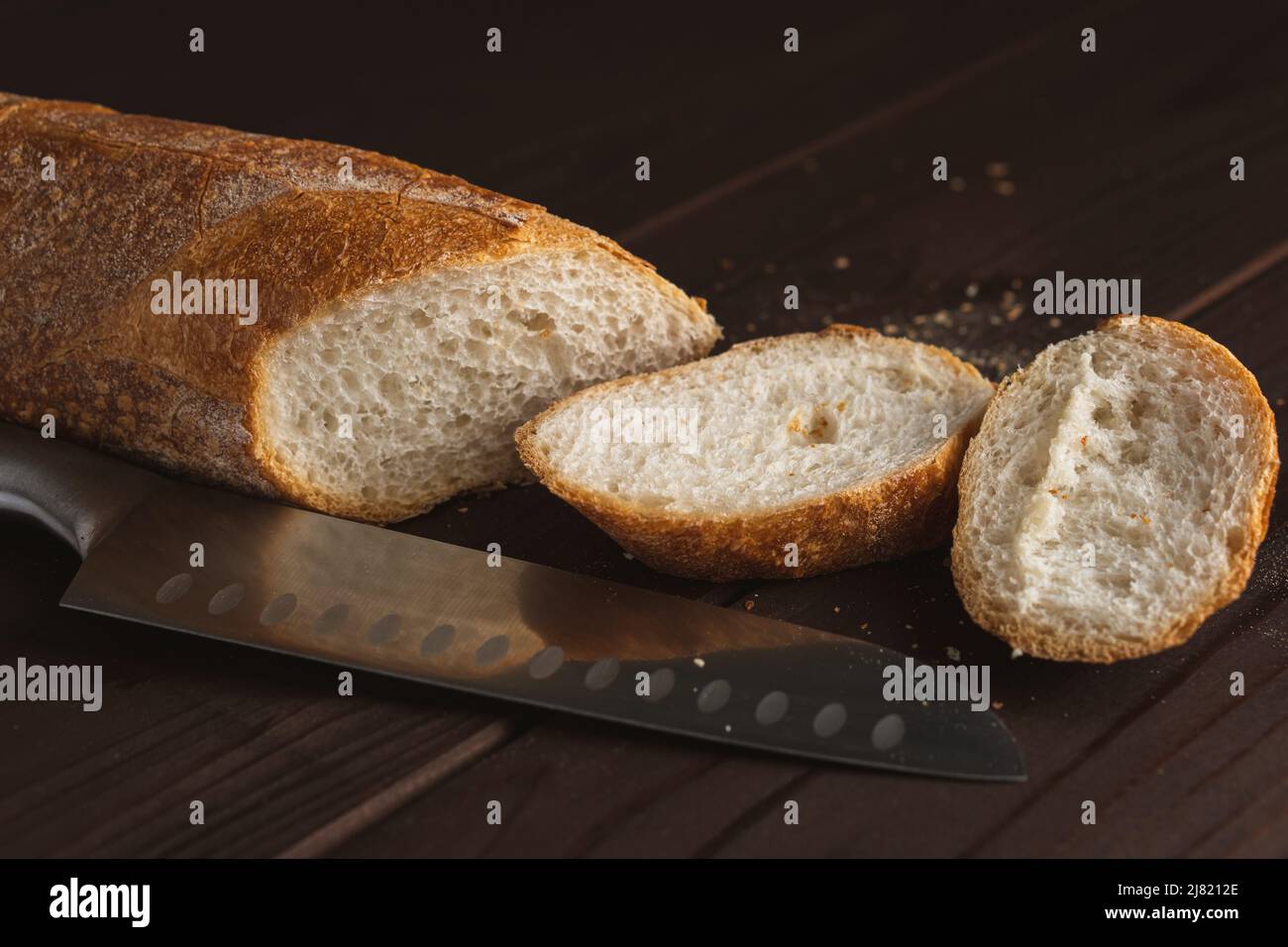 Tagliare a pezzetti il pane fresco di grano. Fette di baguette francese e coltello su tavola di legno Foto Stock