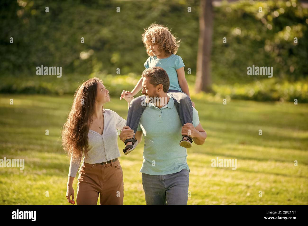 Felice famiglia di madre e padre che porta bambino ragazzo sulle spalle estate all'aperto, adottivo Foto Stock