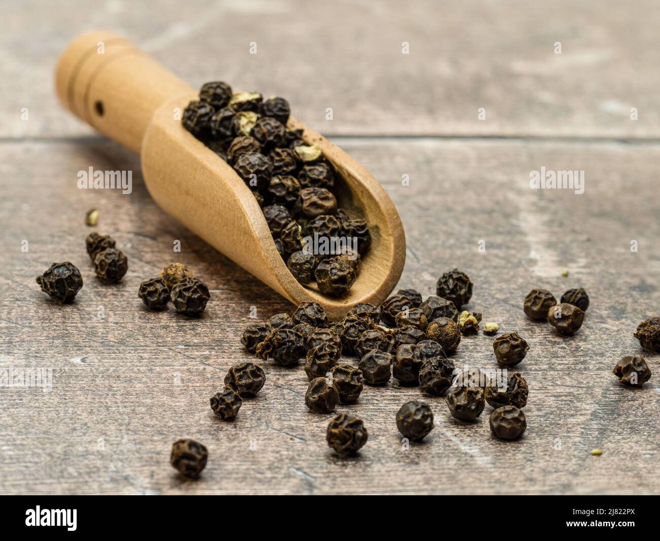 Cucchiaio di legno contenente pepe nero intero isolato su sfondo bianco Foto Stock