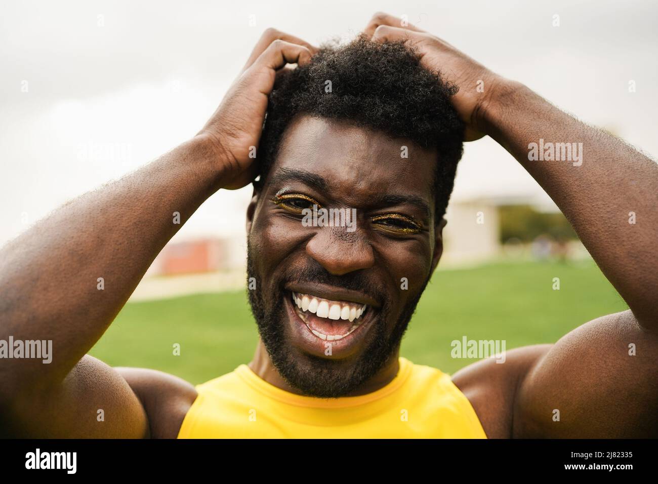 Uomo transgender africano con trucco sorridente sulla macchina fotografica all'aperto - fuoco sul volto Foto Stock