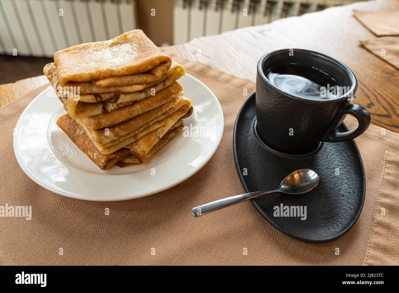 Impila di pancake, tazza scura e caffettiera su un tavolo di legno. Vista laterale fuoco selettivo Foto Stock