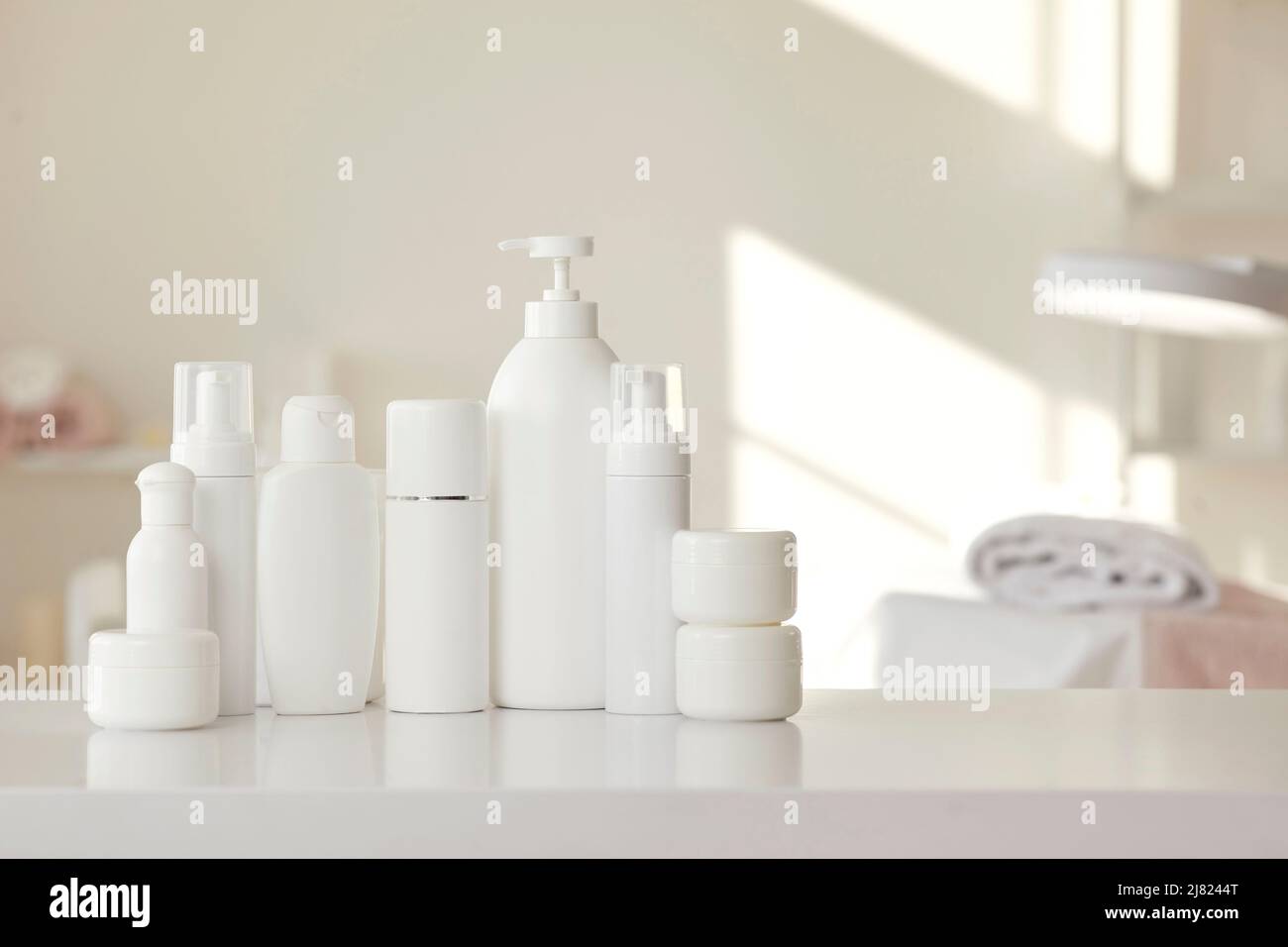 Bottiglie e vasetti in mockup bianco con prodotti per la cura della pelle posti sul tavolo nel salone di bellezza Foto Stock