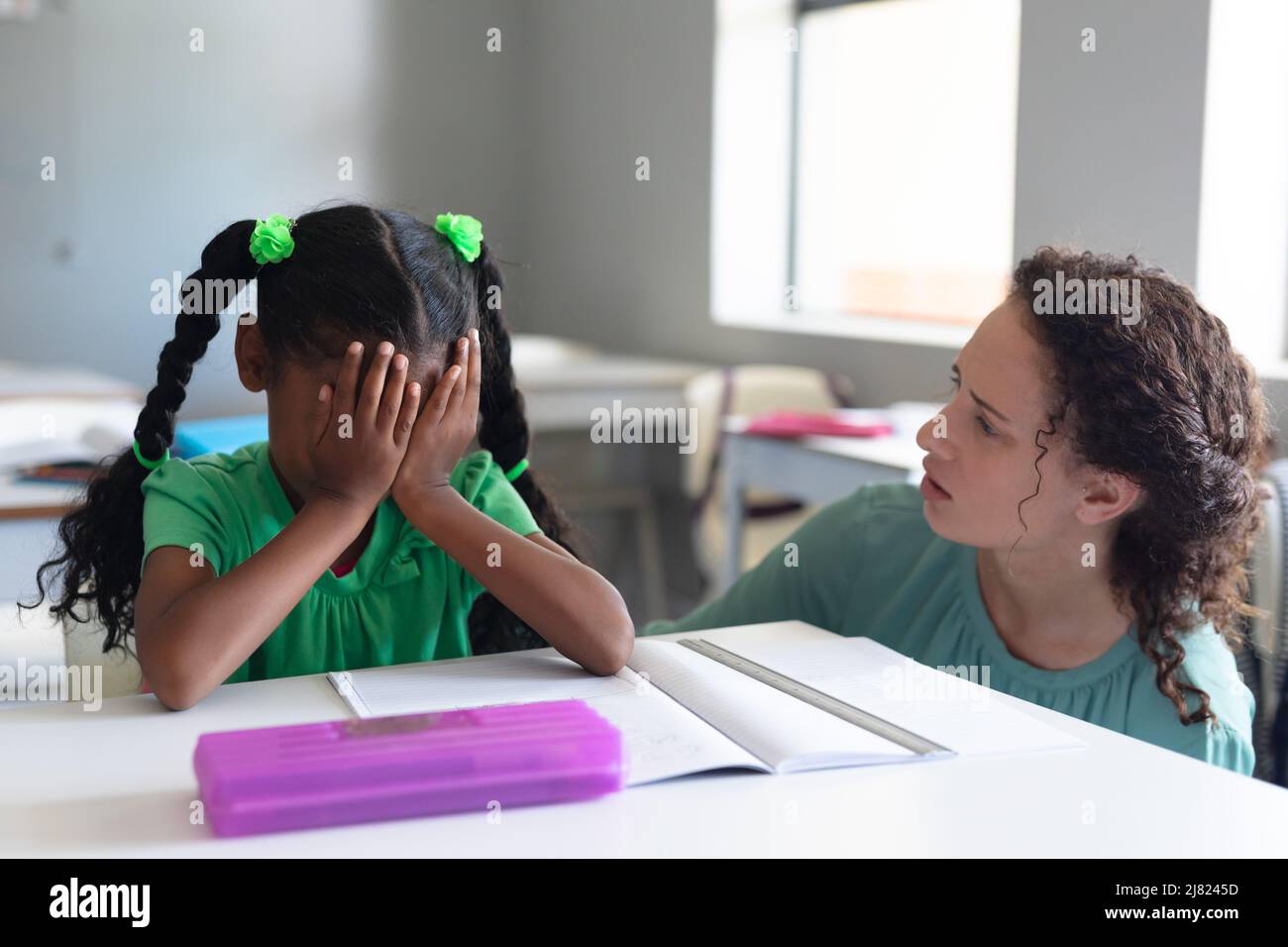 Giovane insegnante caucasica che guarda la studentessa elementare afroamericana con mano sul volto Foto Stock