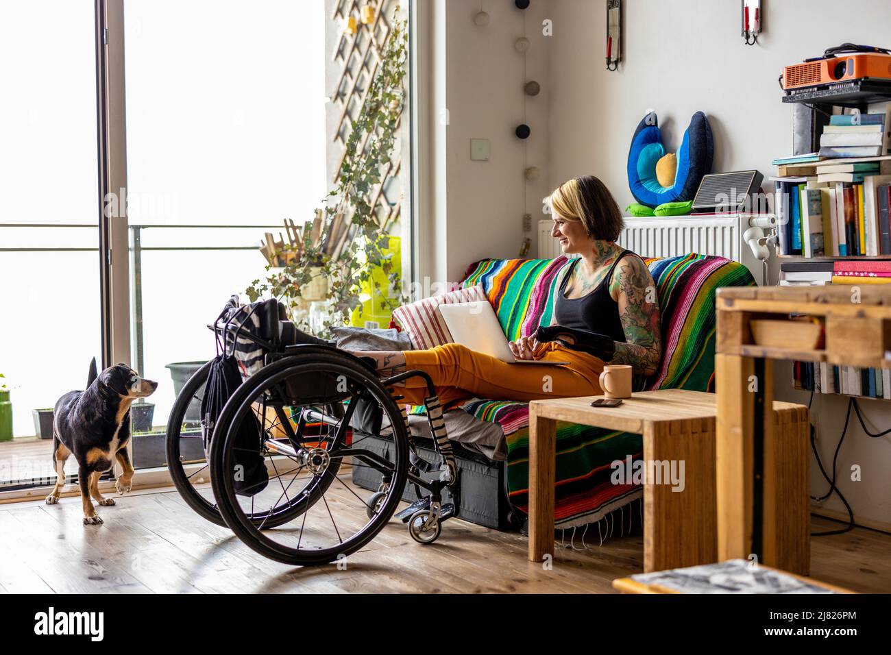 Giovane donna con disabilità che utilizza il computer portatile mentre si siede sul divano a casa Foto Stock