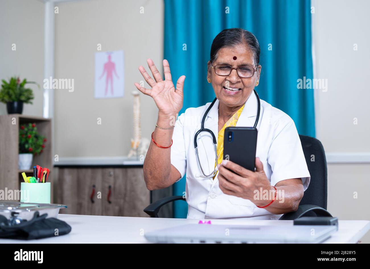 Medico senior in videochiamata con il paziente sul telefono cellulare in ospedale - concetto di consulenza virtuale, assistenza sanitaria e comunicazione Foto Stock