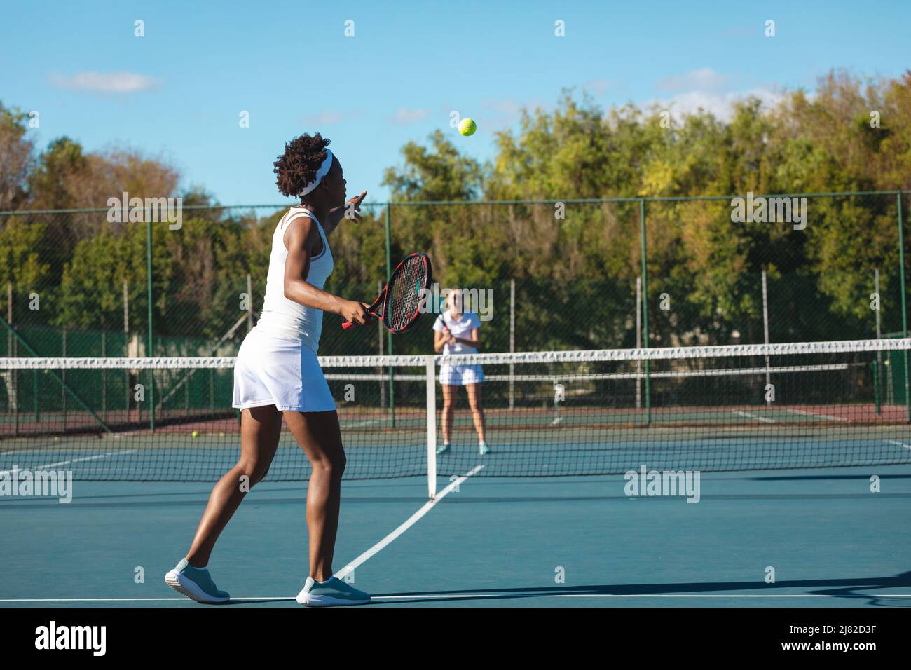 Atleta afro-americana che gioca a tennis con concorrente caucasico in campo il giorno di sole Foto Stock