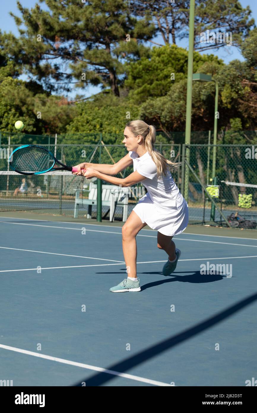 Fidata giovane donna caucasica giocatore di tennis che colpisce palla con racket in campo in giorno di sole Foto Stock