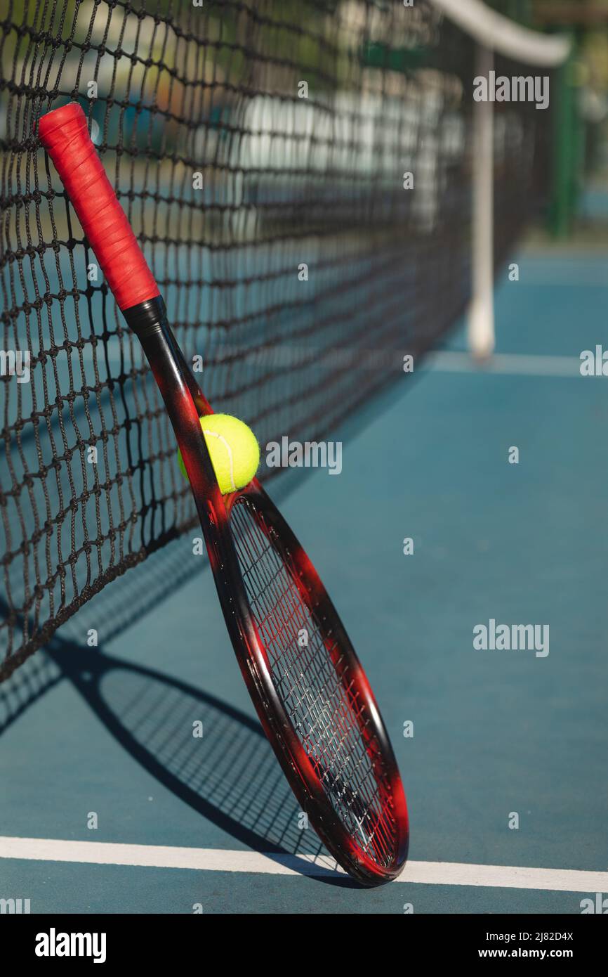 Palla con racket rosso appoggiato su rete da tennis in campo durante la giornata di sole Foto Stock