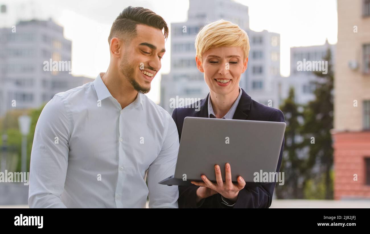 Seri diversi colleghi coppia multirazziale arabo ispanico uomo e donna caucasica in piedi vicino business center in strada guardando il computer Foto Stock