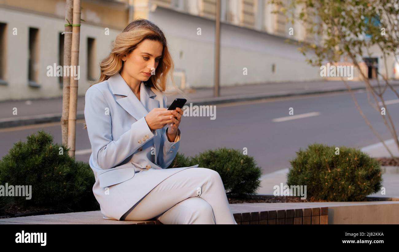 Giovane bella caucasica donna d'affari studente seduto all'aperto in città sfondo di strada guardando il telefono cellulare utilizza smartphone per lo shopping Foto Stock