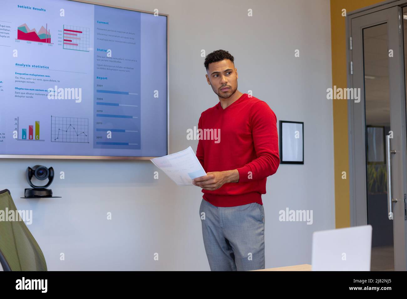 Consigliere maschio ispanico in possesso di documento guardando via mentre in piedi da business plan sul posto di lavoro Foto Stock