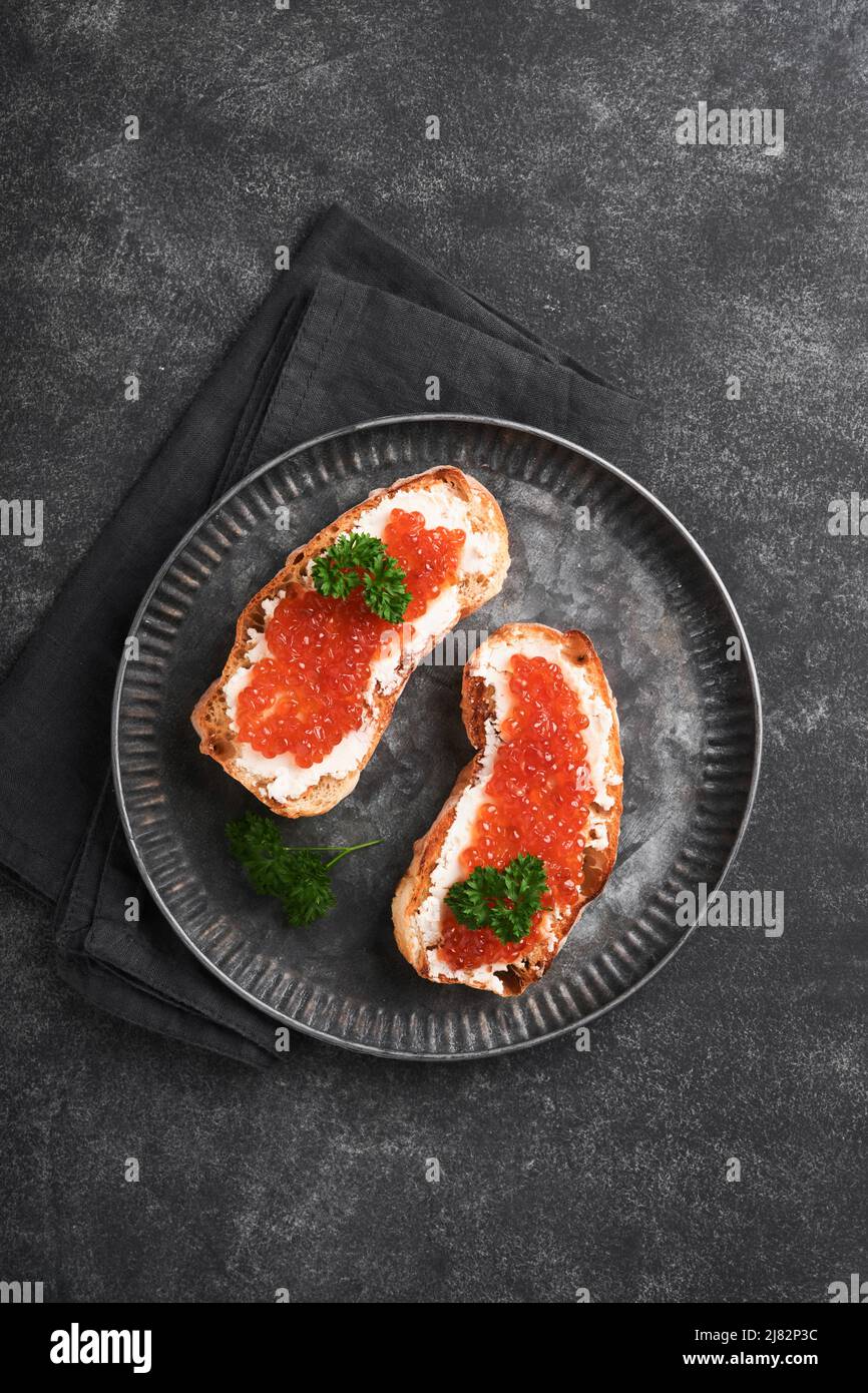 Due dandwiches con caviale rosso. Caviale rosso salmone in ciotola e sandwich server su vecchio piatto di ferro su sfondo vecchio tavolo nero. Vista dall'alto. Spazio di copia. Foto Stock