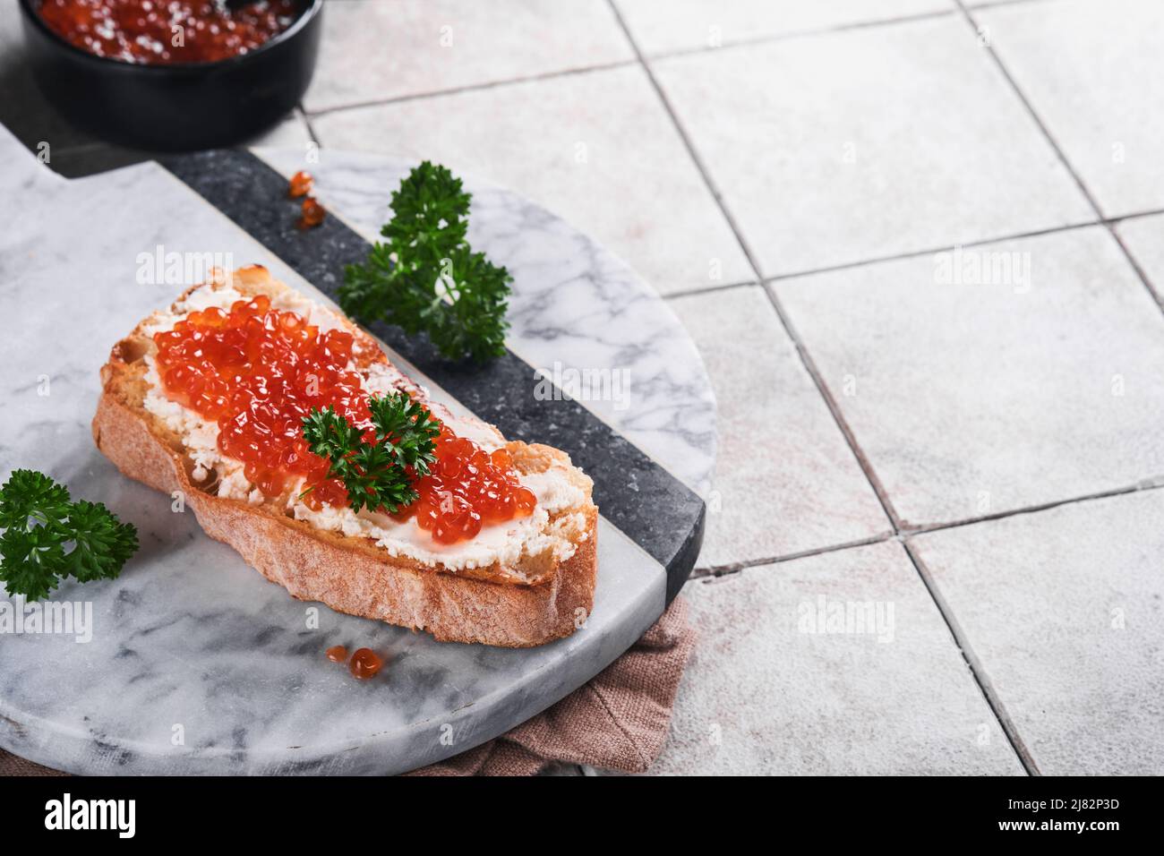 Panini rossi caviale. Caviale rosso salmone in ciotola e sandwich su piastra di marmo su vecchio sfondo grigio cracking tavolo piastrelle. Vista dall'alto. Spazio di copia. Foto Stock