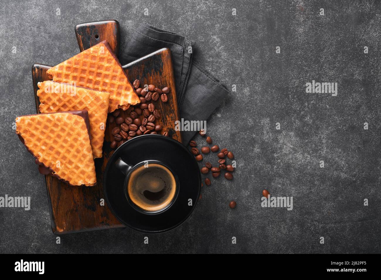 Caffè e waffle olandesi. Caffè espresso e cialde olandesi o biscotti con cialde sciroppate e cioccolato vecchio su un tavolo di cemento nero. Cialda perfetta Foto Stock