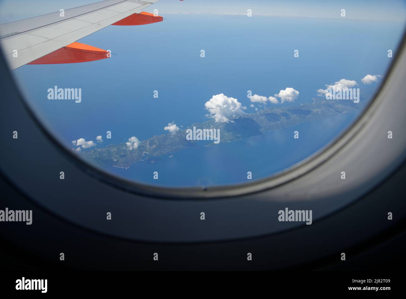 Vista di un'isola croata dalla finestra di un aereo. Il mare Adriatico tra Italia e Croazia. Piccole nuvole che si ergono sopra l'isola. Foto Stock