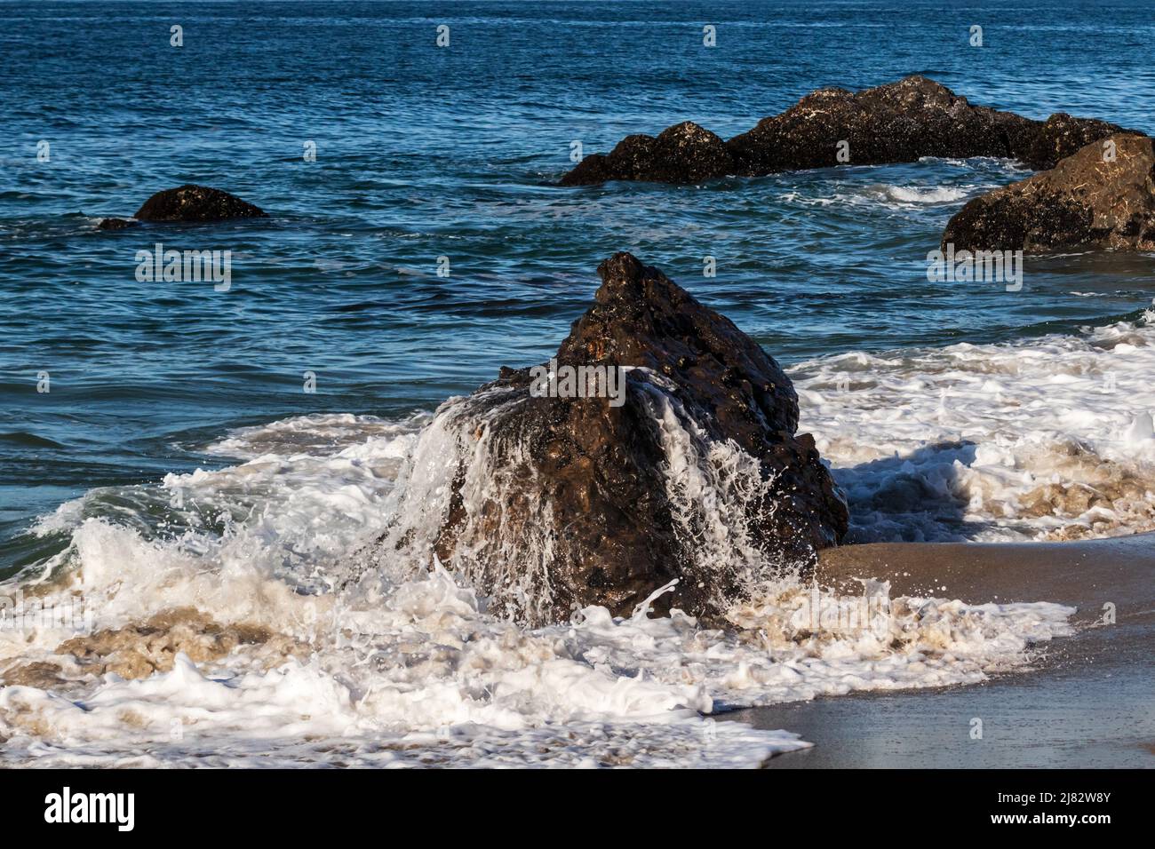 Acqua che sgocciola da una roccia esposta a bassa marea, presso la spiaggia vicino Malibu, California. Blu Oceano Pacifico sullo sfondo. Foto Stock