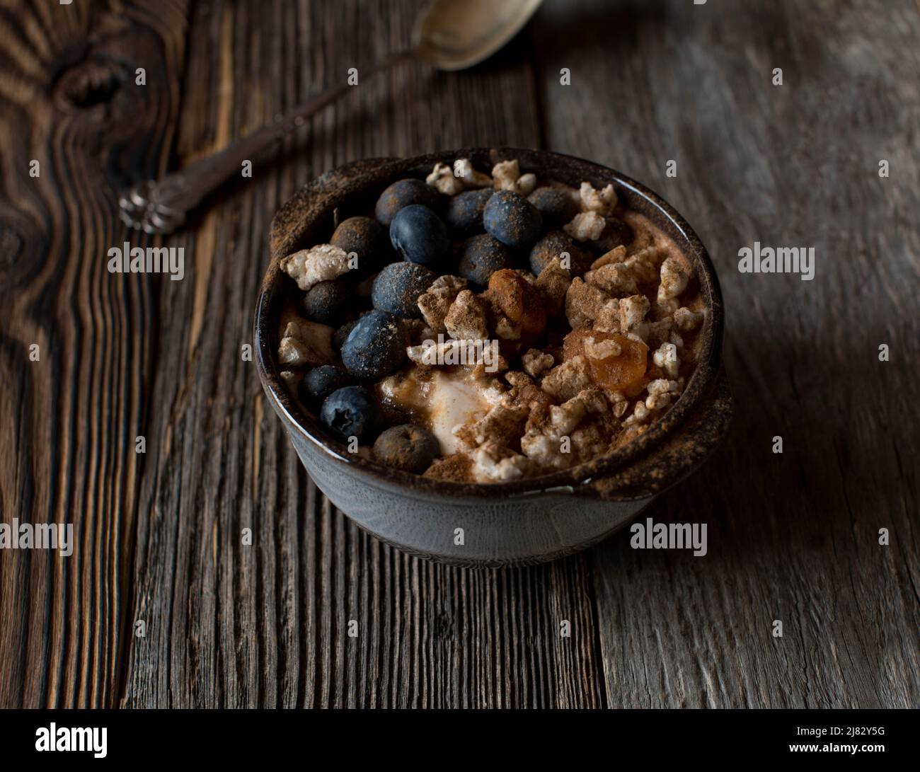 Recipiente per la colazione con yogurt, riso marrone soffiato, mirtilli, zucca e cannella. Isolato su tavolo di legno con spazio per la copia Foto Stock