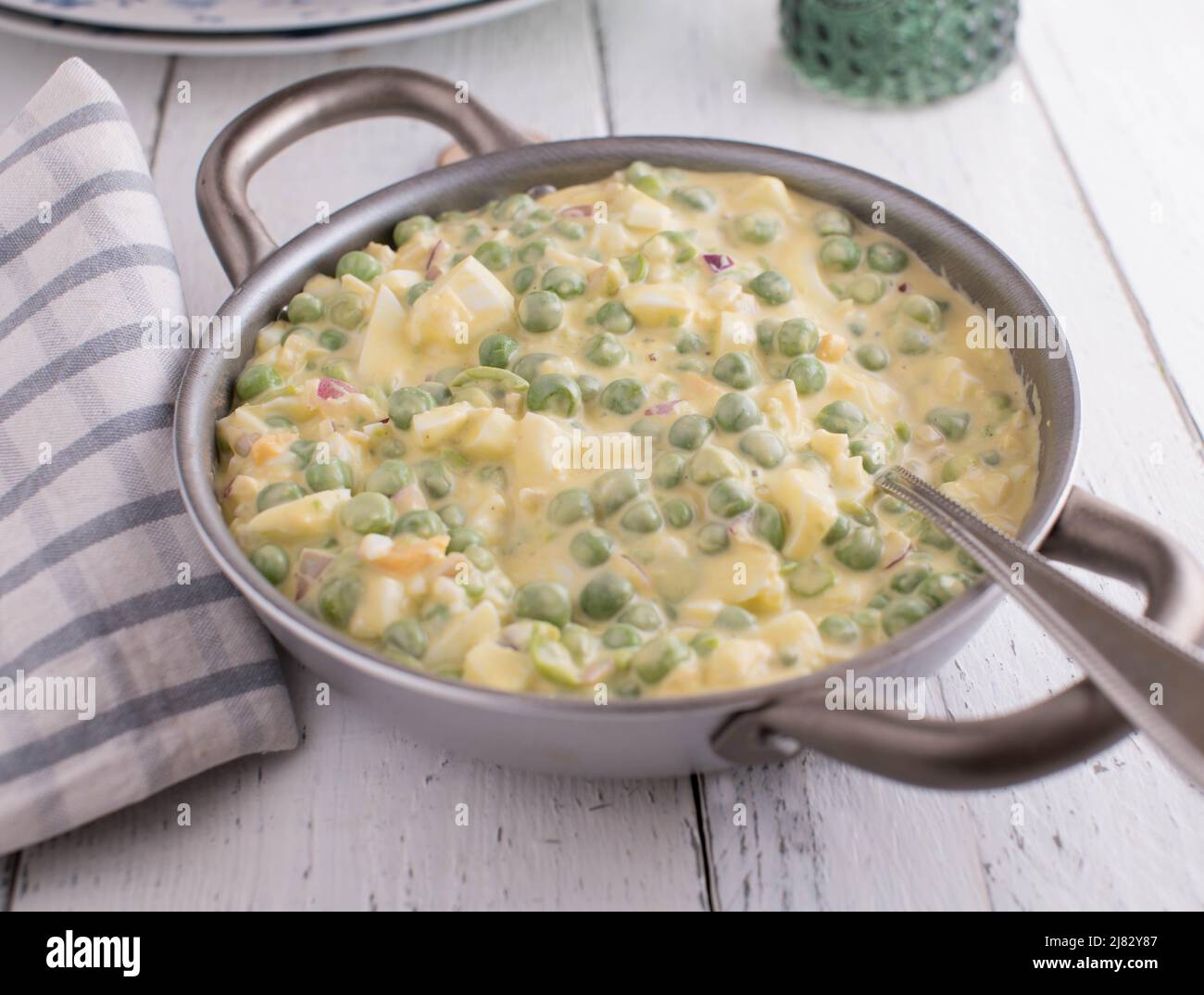 Insalata di uova con piselli verdi, cipolle rosse e maionese in un recipiente con cucchiaio Foto Stock