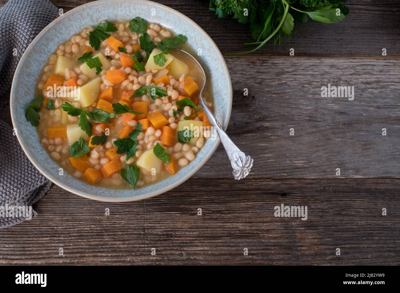 Zuppa di fagioli vegani con verdure e patate. Servito in una ciotola con cucchiaio su tavola di legno. Vista dall'alto con spazio di copia Foto Stock